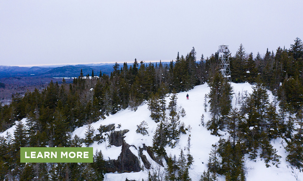 An aerial view of a firepower peak and a hiker in the winter with a Learn More button.